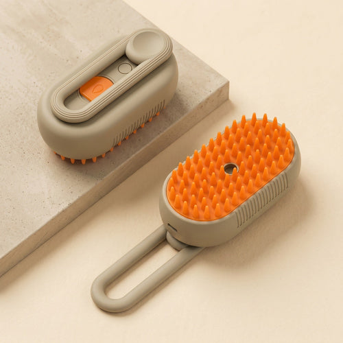 Khaki cat steam brush shown folded on a stone plinth and lying with its handle extended, orange silicone bristle pad facing upHand holding the white cat steam brush, showing its soft silicone bristle pad in a bright living room