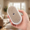 Hand holding the white cat steam brush, showing its soft silicone bristle pad in a bright living room
